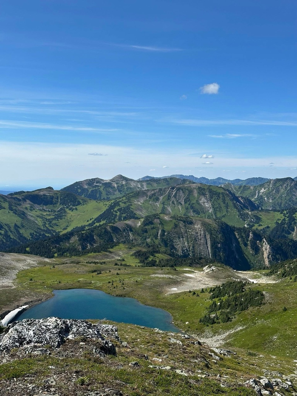A blue alpine lake below green slopes and rocky mountain ridges, viewed from Torpy Mountain