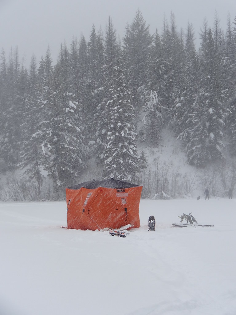 Orange ice-fishing shelter and snowshoes against snowy forest at Eskers